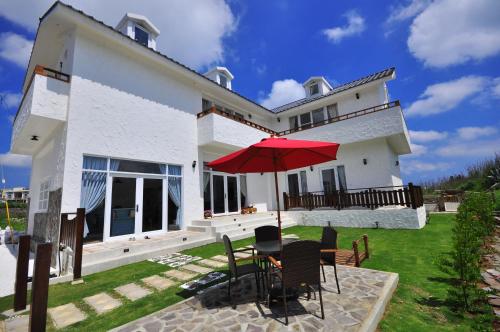 a white house with a table with a red umbrella at Sea Daughter's Homestay in Huxi
