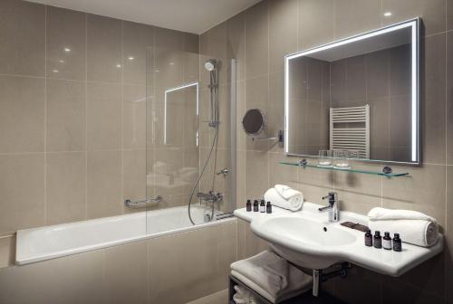 een badkamer met een wastafel, een bad en een spiegel bij Michelangelo Grand Hotel in Praag