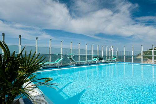 a swimming pool with chairs and the ocean in the background at Hotel Napoleon in Gabicce Mare