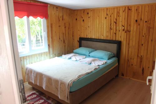 1 dormitorio con 1 cama en una habitación con paredes de madera en SaklıBahçe Pension, en Cıralı