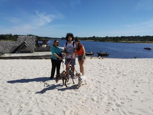 three women standing on the beach with a dog on a leash at Playa, bosque y lago in Montevideo