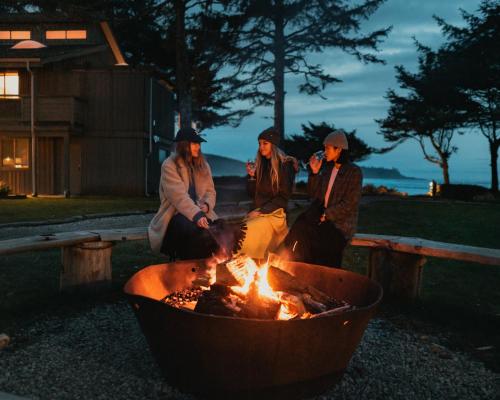 a group of three people sitting around a fire at Pacific Sands Beach Resort in Tofino