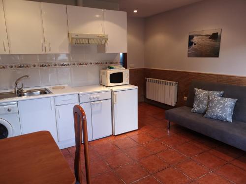a kitchen with white cabinets and a couch and a microwave at Apartamentos La Tarazana 4 in La Pereda de Llanes