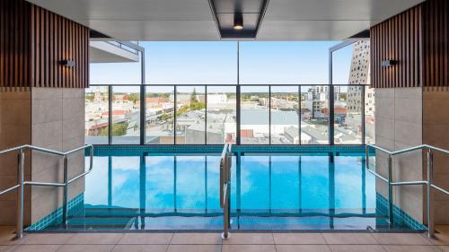 a swimming pool in a building with a large window at Avani Adelaide Residences in Adelaide