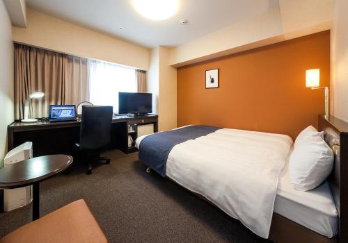 水戸市にあるダイワロイネットホテル水戸のベッド、デスク、コンピュータが備わるホテルルームです。