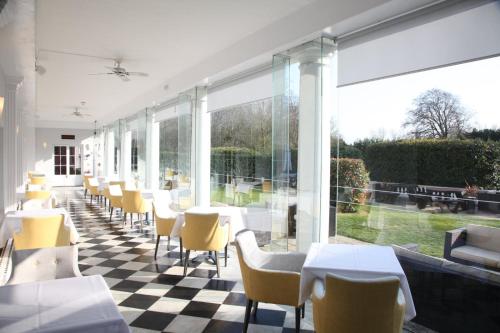 a restaurant with white tables and yellow chairs and windows at Manor Of Groves Hotel, Golf & Health Club in Sawbridgeworth