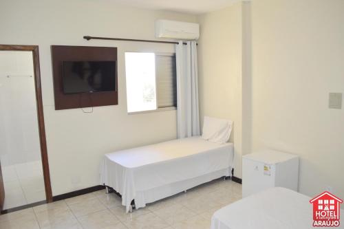 Habitación con cama blanca y TV. en Hotel e Restaurante Araújo, en Montes Claros