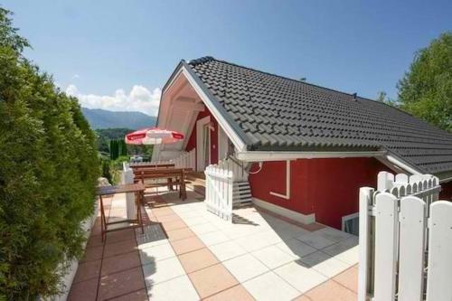 una pequeña casa roja con una mesa y una sombrilla en Faakersee Seahouse mit Privat Strand -Only Sa-Sa, en Faak am See