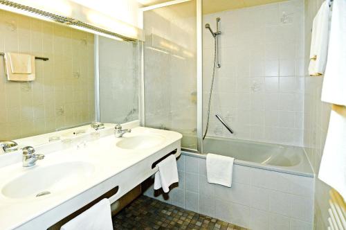 uma casa de banho com 2 lavatórios, um chuveiro e uma banheira. em Hotel Café Schlack em Tuttlingen