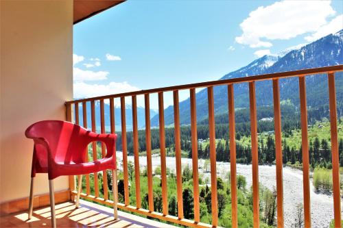 a red chair on a balcony with a view of mountains at La Vaca India Manali in Manāli