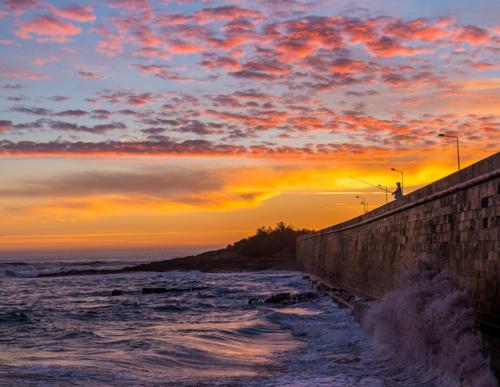a sunset over the ocean with a wall at Paradise Suites in Carcavelos
