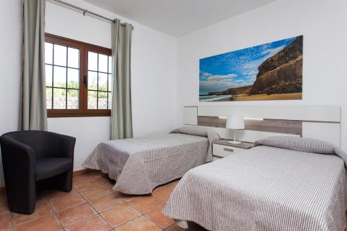 a bedroom with two beds and a chair and a window at Villas & Apartamentos Tao Mazo in Lajares