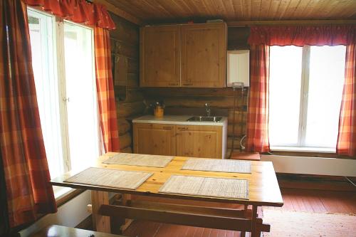 a kitchen with a wooden table and two windows at Paltto Elämysretket in Lemmenjoki