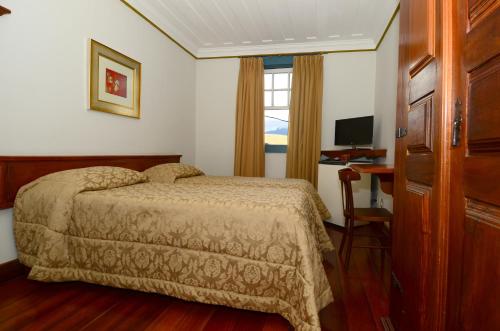 a bedroom with a bed and a desk and a window at Hotel Pousada Casa Grande in Ouro Preto