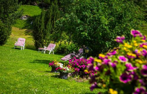 zwei Stühle im Garten mit Blumen im Gras in der Unterkunft Hotel Alpenhof in Saas-Almagell