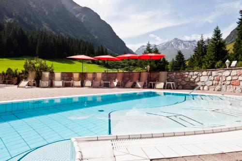a swimming pool with red umbrellas and a mountain at Sport- und Vitalhotel Seppl in Sankt Leonhard im Pitztal