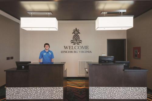 a man standing behind a counter in a room with a welcome sign at La Quinta by Wyndham Lynchburg at Liberty Univ. in Lynchburg
