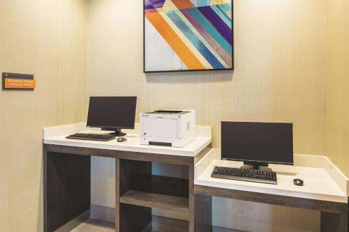 a desk with two computer monitors and a printer at La Quinta Inn & Suites by Wyndham Atlanta South - McDonough in McDonough