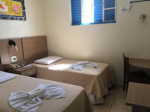 a room with two beds and a table and a window at Hotel Vila Rica in Alfenas