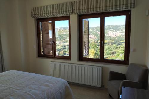a bedroom with three windows and a bed and a chair at Villa HERMIONA in Kouklia
