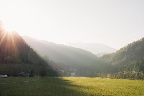 a green field with the sun shining on a mountain at Trolltunga/Folgefonna Camp house in Jondal