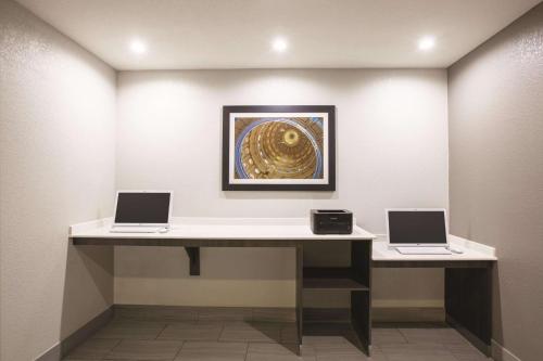 two laptops on a desk in a room with a painting at La Quinta by Wyndham Mansfield TX in Mansfield