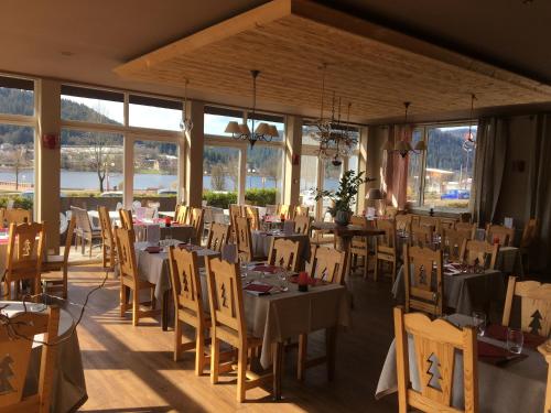 uma sala de jantar com mesas, cadeiras e janelas em Le Ptit Hotel du Lac em Gérardmer