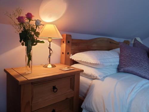 a bed with a vase of flowers on a night stand with a lamp at Kirk Cottage in Tobermory