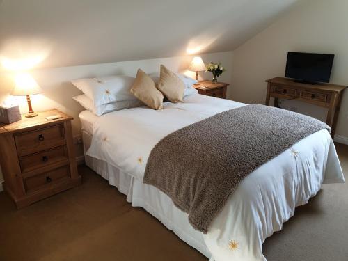 Cette chambre comprend un lit blanc avec des oreillers et une télévision. dans l'établissement Kirk Cottage, à Tobermory