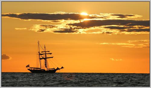 a boat in the ocean at sunset at Exklusiver Bungalow direkt am Strand in Dranske