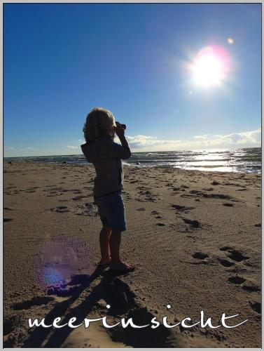 a child standing on the beach taking a picture of the ocean at Exklusiver Bungalow direkt am Strand in Dranske