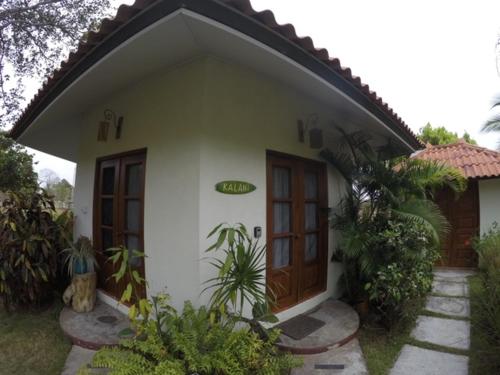 a white house with a brown door and some plants at Cabañas La Casa de Pucha in Pedasí Town