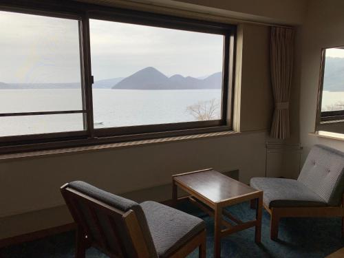 a room with two chairs and a table and a large window at Toya Kanko Hotel in Lake Toya