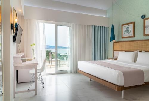 a bedroom with a bed and a desk and a balcony at Zoe Hotel, Trypiti Beach Resort & Hive water park in Limenaria