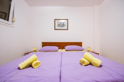 a bedroom with two beds with purple sheets and yellow pillows at APARTMANI Mila in Podstrana