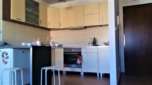 a kitchen with white cabinets and an oven and stools at Sympatyczny Apartament in Gdańsk