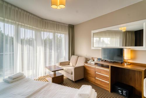 a hotel room with a bed and a television and a chair at Hotel White in Krynica Morska