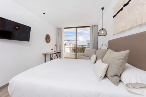 a white bedroom with a large bed and a tv at Hotel Sa Clau by Mambo in San Antonio