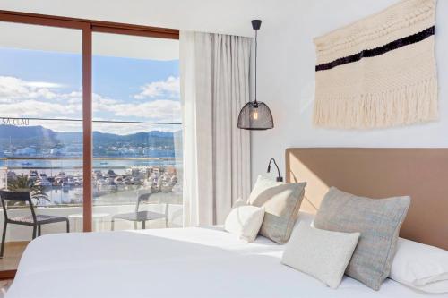 サンアントニオにあるHotel Sa Clau by Mamboのベッドと大きな窓が備わるホテルルームです。