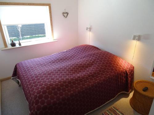 a bedroom with a bed with a purple comforter and a window at Fin lejlighed med lukket have in Skagen