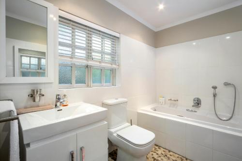 a white bathroom with a toilet and a sink and a tub at Quainton Cottages in Hermanus