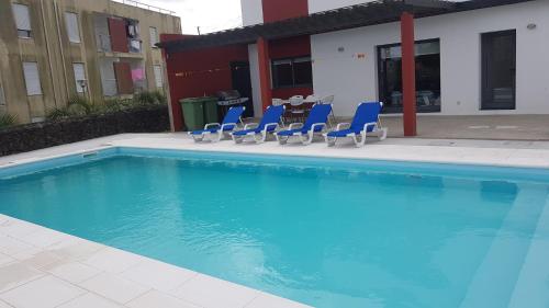 a swimming pool with blue chairs and a table at Deluxe Home Praia do Populo in Cabouco