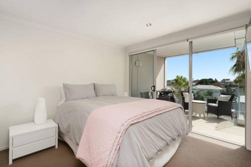 a white bedroom with a bed and a balcony at Awesome Downtown Location - park the car and walk to everything ! in Mount Maunganui