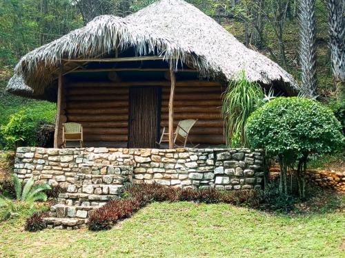 a log cabin with a thatched roof and a stone wall at cabins sierraverde huasteca potosina "cabaña la ceiba" in Damían Carmona