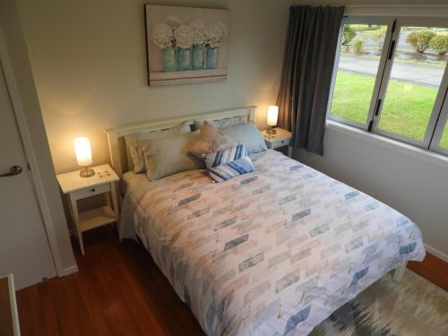 a bedroom with a bed with two tables and two lamps at Thistle Do Beach Bach in Ruakaka