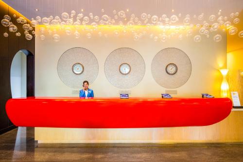 a woman standing behind a large red desk with clocks on the wall at ibis Mall Avenue Dubai in Dubai