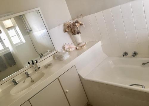 La salle de bains blanche est pourvue d'une baignoire et d'un lavabo. dans l'établissement On The Square Luxury Apartment, à Simonʼs Town