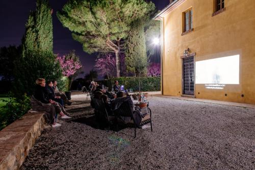 a group of people sitting on benches outside a building at night at Villa Aia Vecchia in Bibbona
