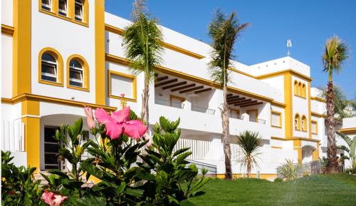 a yellow and white building with palm trees and pink flowers at Apartamento Playa de Punta Candor in Rota