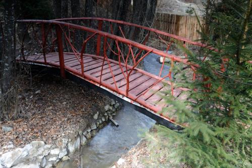 a red metal bridge over a stream of water at Szarvas Vendeghaz in Izvoru Mureşului